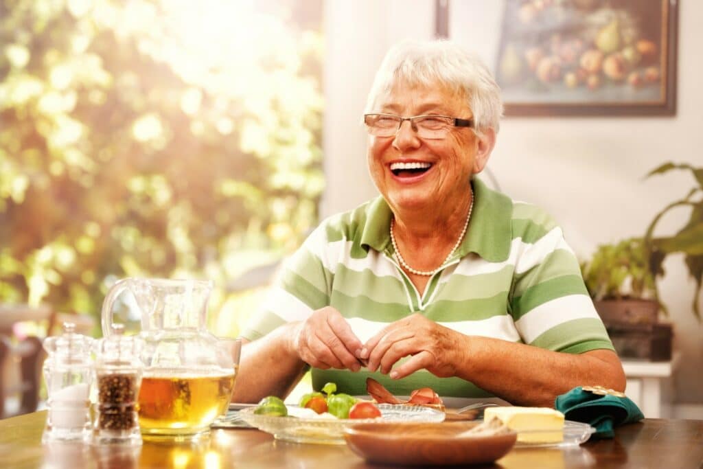 Elderly woman smiling, enjoying breakfast in the sun during her Respite stay at Hallmark Care Homes.