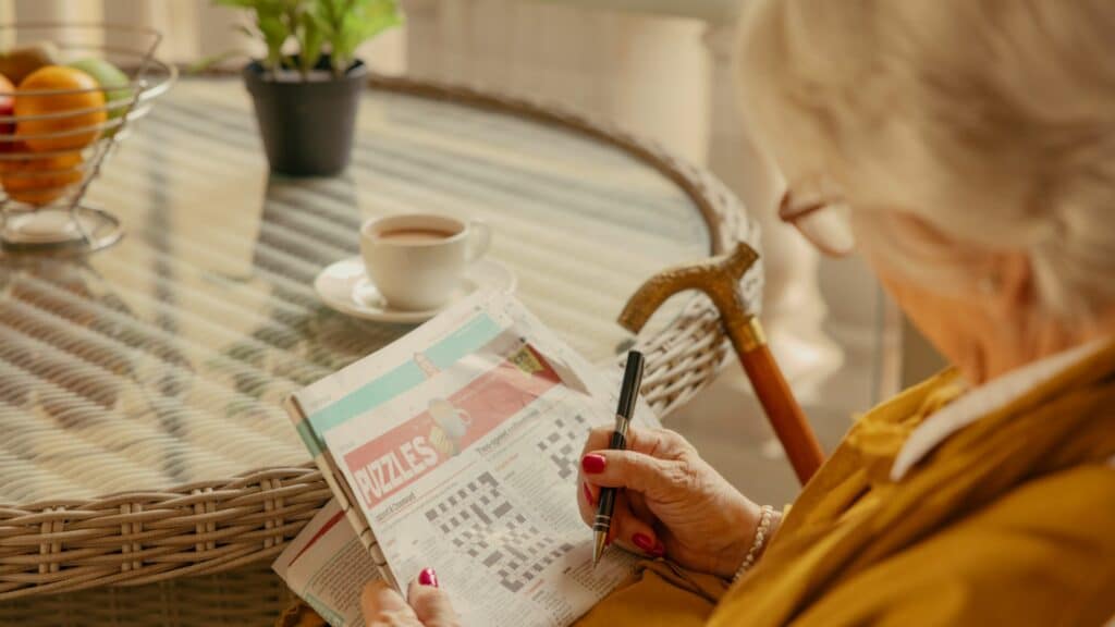 Elderly woman doing crossword puzzle with coffee.