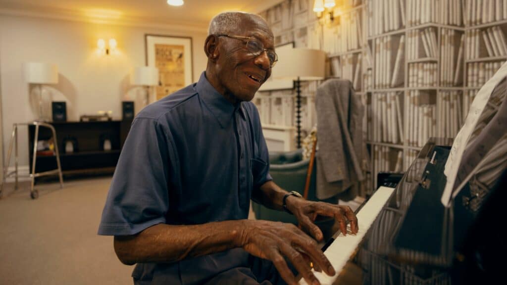 Elderly man playing piano and smiling indoors.