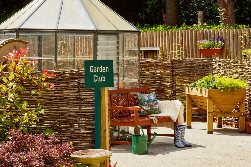 Outdoor garden club area with bench, plants, and greenhouse.