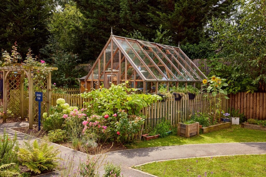 Wooden greenhouse in a garden with flowers.