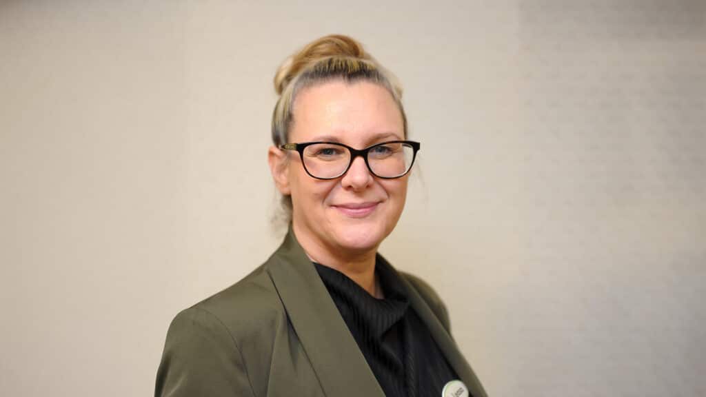 Smiling person in glasses and a green blazer.