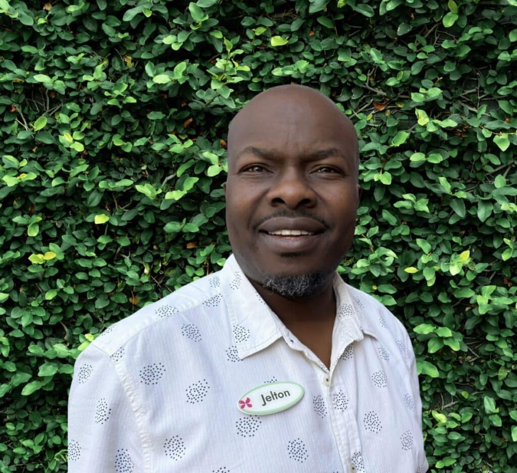 Person in white shirt against green leafy background.