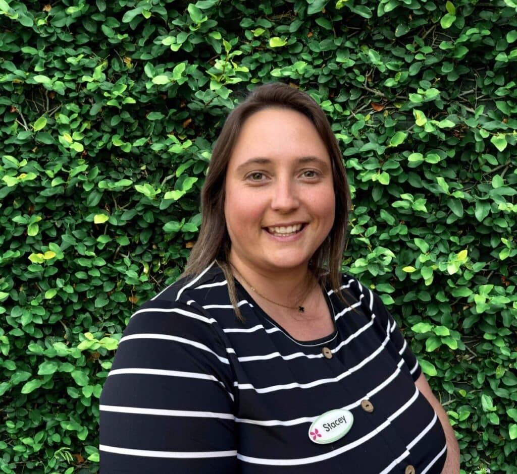 Person smiling in front of a green leafy background.