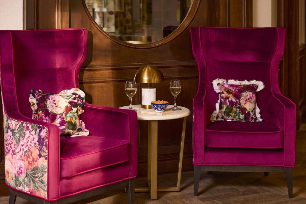 Two pink armchairs with floral cushions, wine, and snacks.