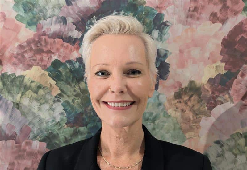 Smiling person in front of colourful abstract background.