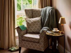 Cosy reading nook with armchair, coffee, and blanket.