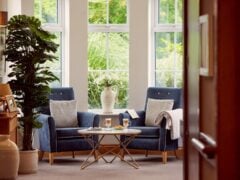 Cosy seating area with large windows, armchairs, and table.