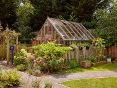 Wooden greenhouse in a garden with flowers.