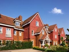 The welcoming entrance of Banstead Manor Care Home, the buildings red façade is in the sun, surrounded by a well established garden.