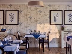 Cosy restaurant with floral wallpaper and framed art.