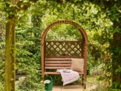 Wooden garden bench with cushion and throw blanket.