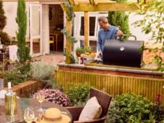 Man cooking barbecue in garden with outdoor seating.