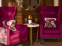 Two pink armchairs with floral cushions, wine, and snacks.