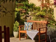 Wooden garden bench with cushion and throw